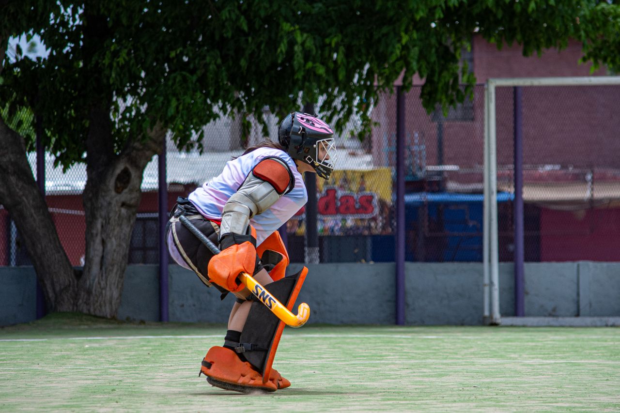 A field hockey goalie in protective gear, ready for action on an outdoor field.