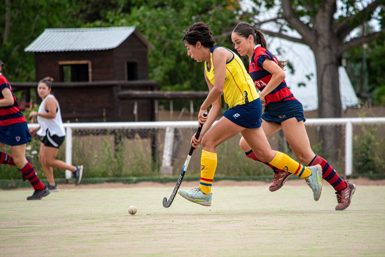 Competitive women's field hockey match outdoors with players in vibrant uniforms.